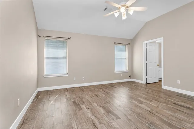an empty room with wooden floor chandelier fan and windows