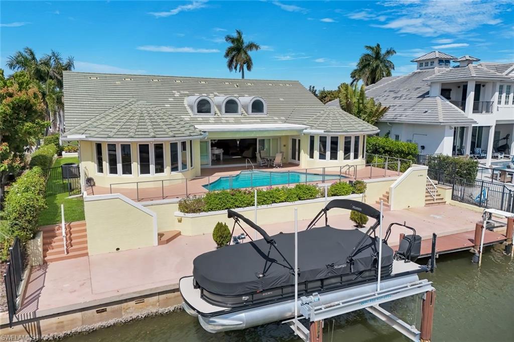 Rear view of property featuring a patio area, boat lift, a tiled roof, and a water view
