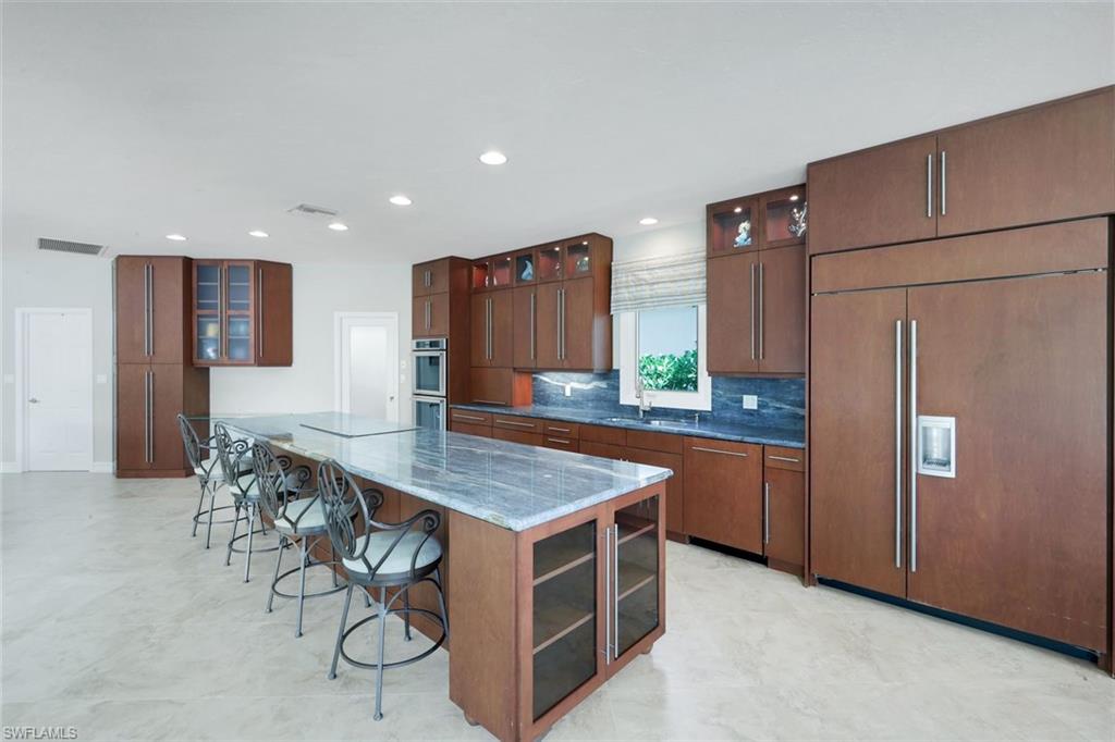 2147 Snook Drive Naples, FL 34102 - Photo 11 of 50 Kitchen featuring glass fronted cabinets, paneled fridge, a kitchen breakfast bar, dark stone countertops, and a large island