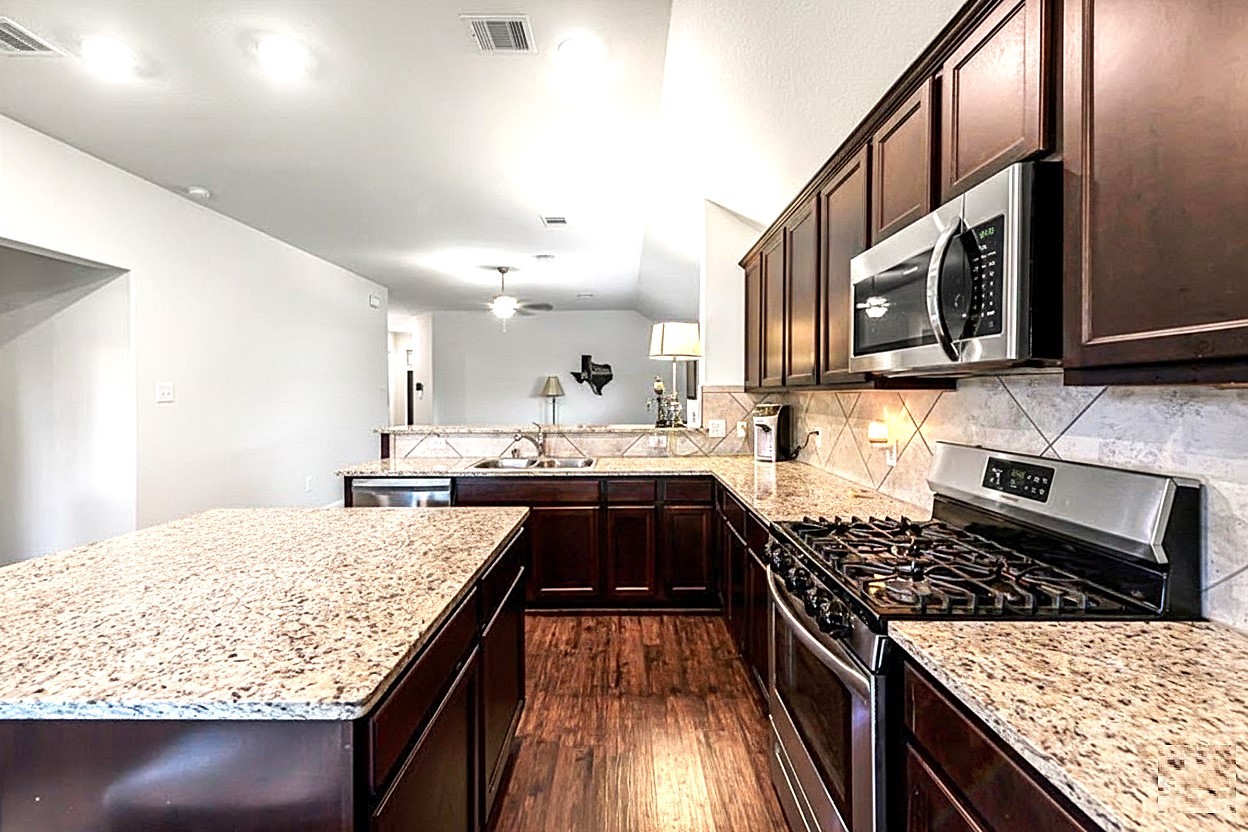 17439 Chester Valley Trail Hockley, TX 77447 - Photo 9 of 22 Spacious kitchen featuring dark wood cabinets, granite countertops, a large island, and modern stainless steel appliances. The open layout and ample lighting create a welcoming atmosphere.