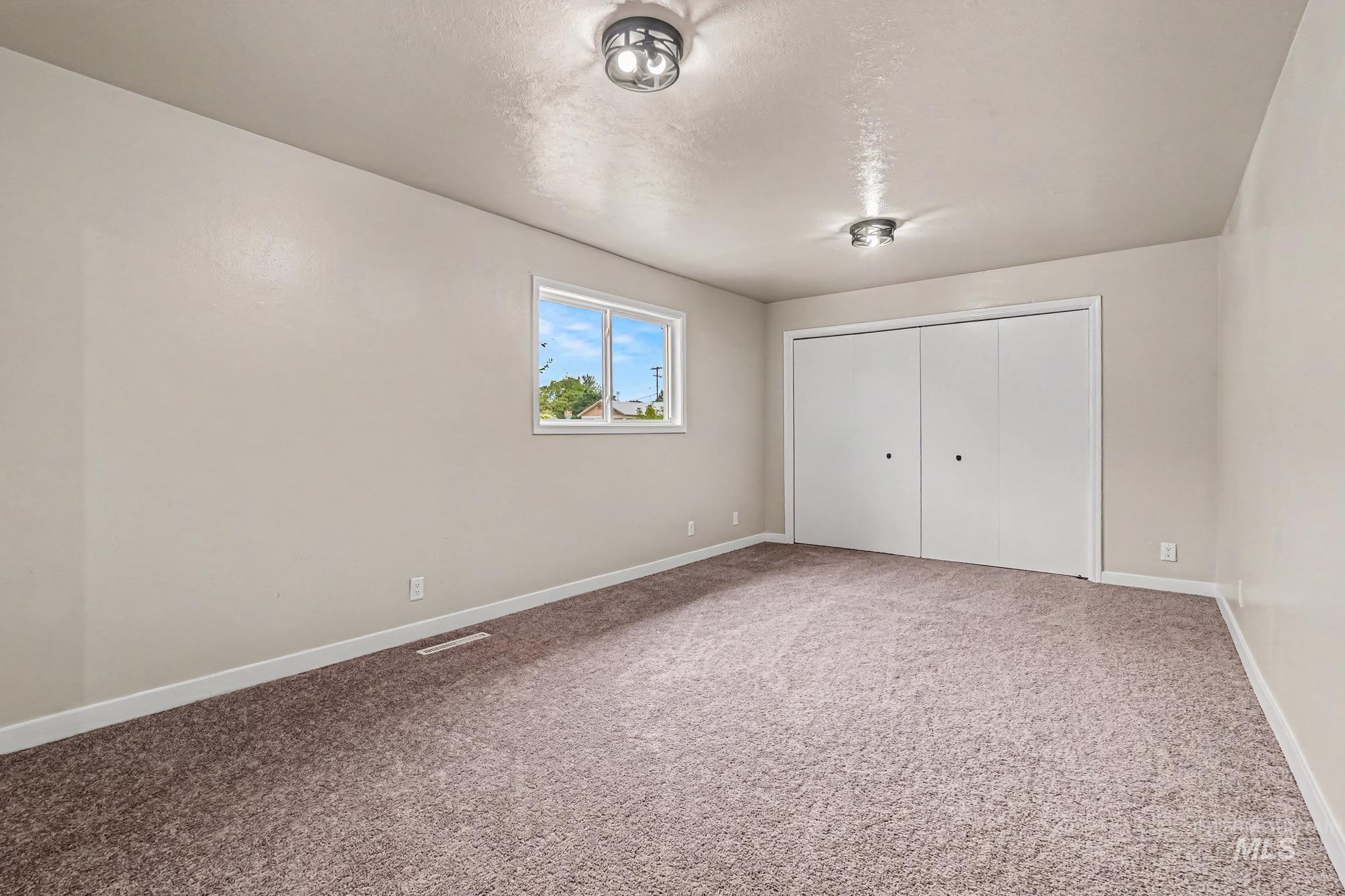 1023 State Street Weiser, ID 83672 - Photo 12 of 25 Spacious room featuring neutral-toned walls, plush carpet flooring, a large window, two flush-mount ceiling lights, and bi-fold closet doors
