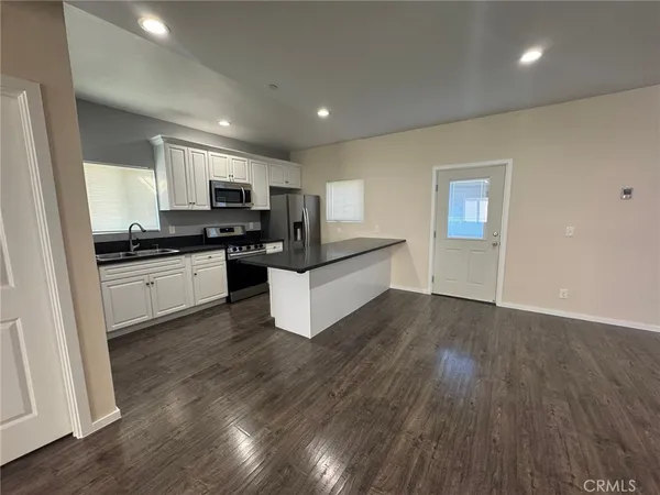 a kitchen with stainless steel appliances granite countertop a stove top oven a sink dishwasher and a refrigerator with wooden floor