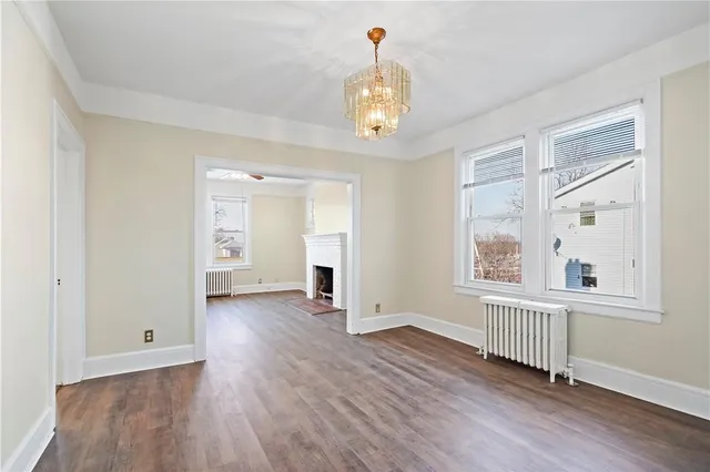 an empty room with wooden floor chandelier and windows