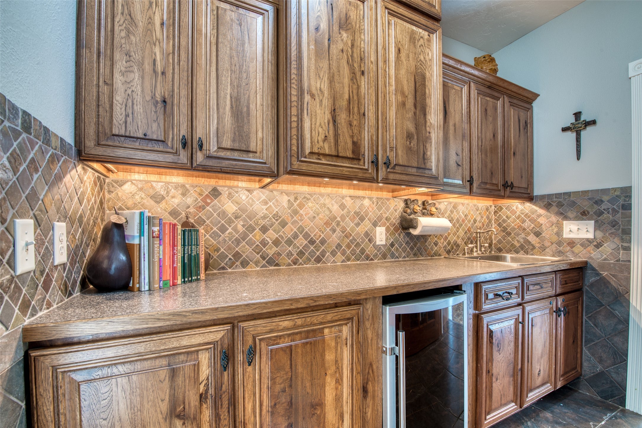 16374 Folsom Road Florence, MT 59833 - Photo 38 of 98 Kitchen featuring beverage cooler, backsplash, brown cabinetry, and light countertops