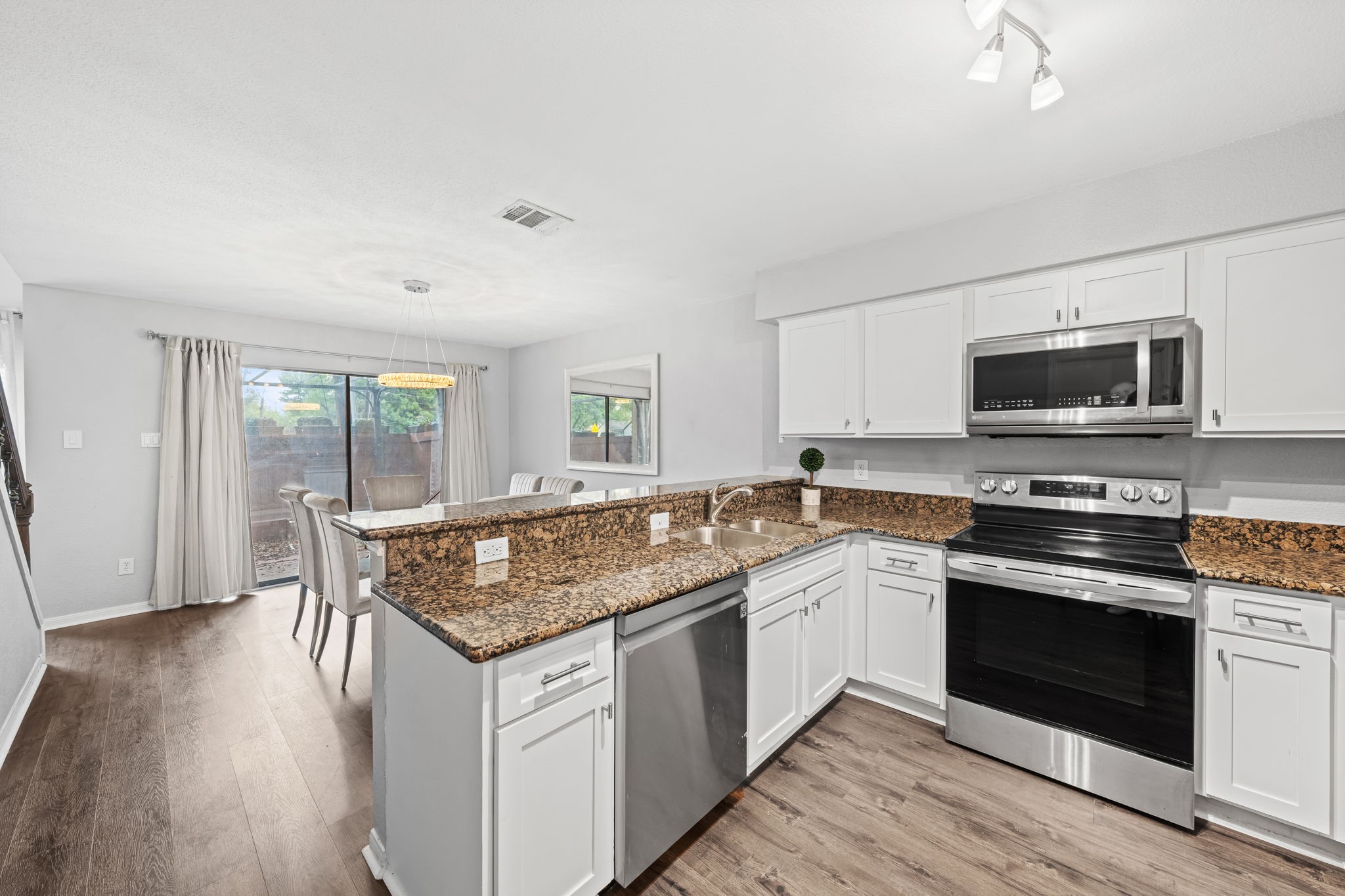 2211 South Kirkwood Road, Unit 1 Houston, TX 77077 - Photo 2 of 16 This kitchen is fully outfitted — white shaker cabinetry with soft-close hardware runs the full perimeter, dark speckled granite countertops cover every surface including the breakfast bar peninsula, and the stainless steel appliance suite includes an electric range, dishwasher, over-range microwave, and a French door refrigerator with water and ice dispenser. The breakfast bar connects directly to the dining area, keeping the kitchen open to the rest of the first floor.