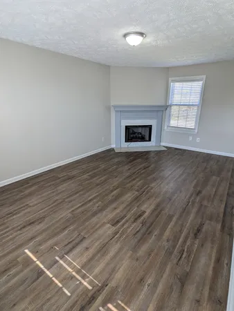 an empty room with wooden floor fireplace and windows