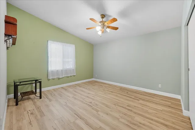 an empty room with wooden floor ceiling fan and windows
