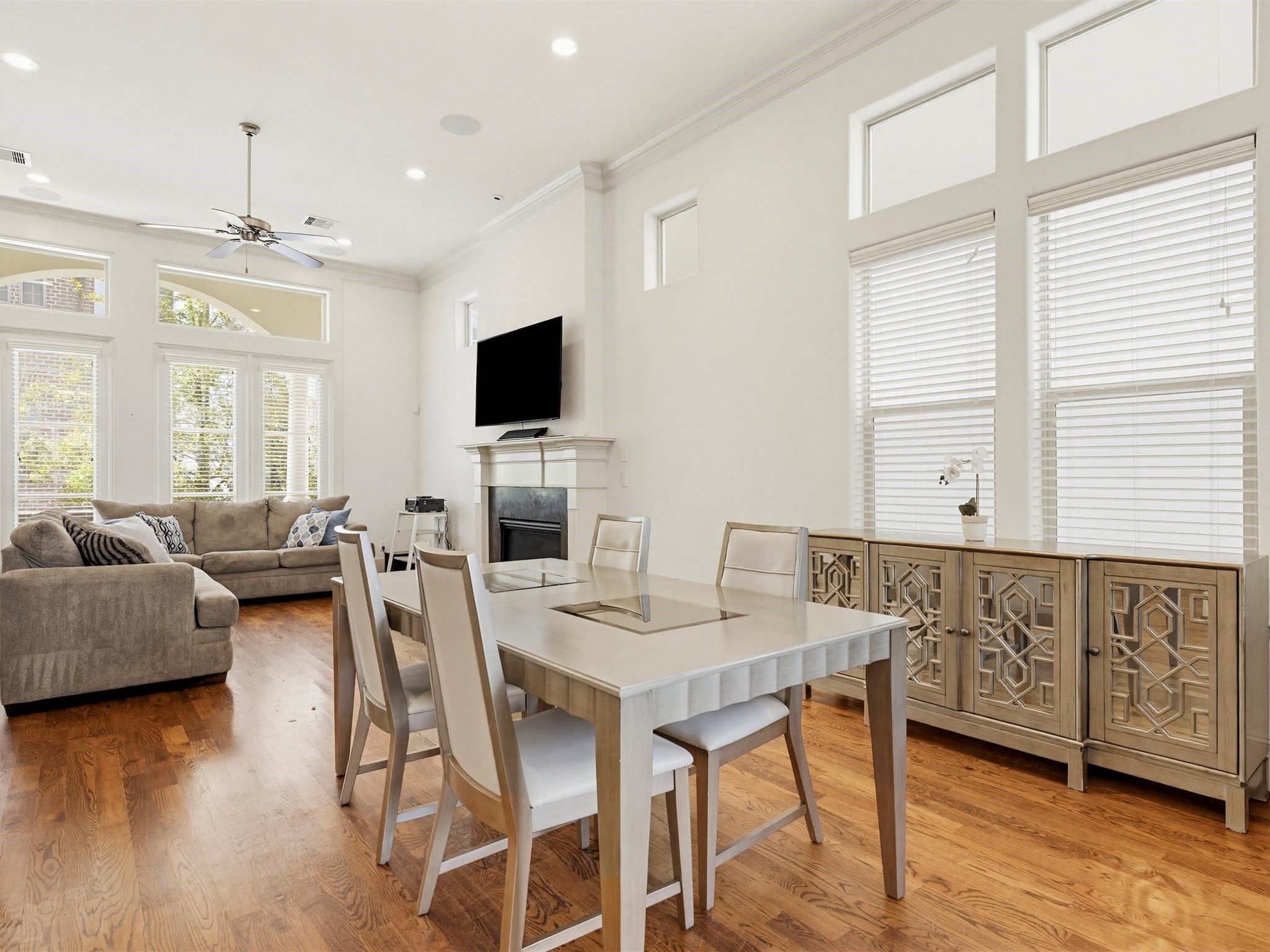 9427 London Bridge Station Houston, TX 77045 - Photo 16 of 30 This bright, open-concept living and dining area features hardwood floors, high ceilings, and large windows for natural light. It includes a cozy sectional sofa, a modern dining set, a wall-mounted TV, and an elegant sideboard.