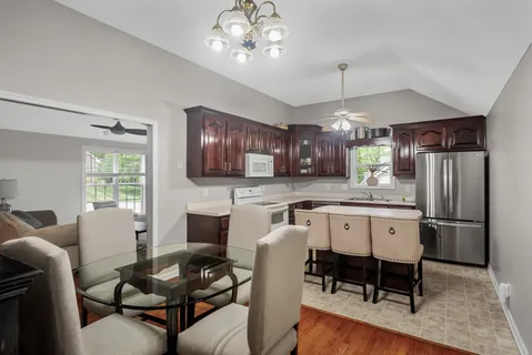 a kitchen with stainless steel appliances kitchen island granite countertop a dining table chairs refrigerator sink and cabinets