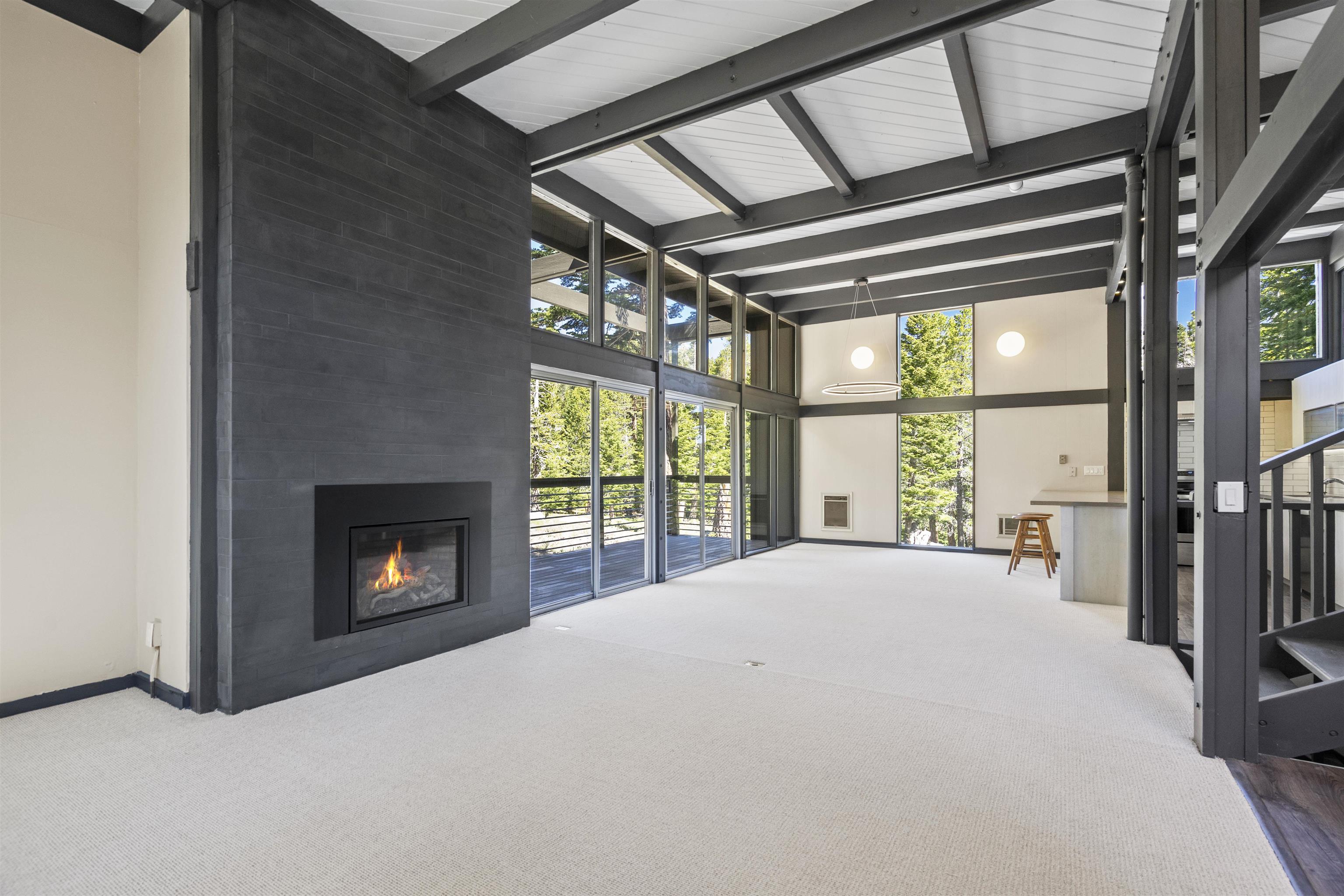 2570 Old Mammoth Road Mammoth Lakes, CA 93546 - Photo 4 of 39 Spacious living area featuring a modern fireplace with a dark-toned surround, expansive windows, a full-height exposed beam ceiling, a built-in counter surface, and light-toned carpeting