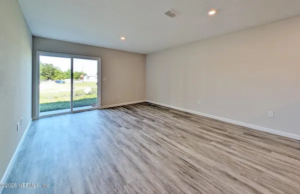 a view of an empty room with wooden floor and a window