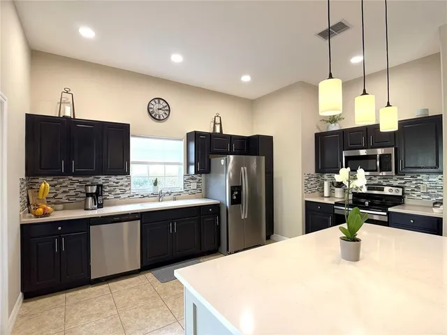a kitchen with stainless steel appliances kitchen island granite countertop a refrigerator a stove top oven a sink dishwasher and wooden cabinets