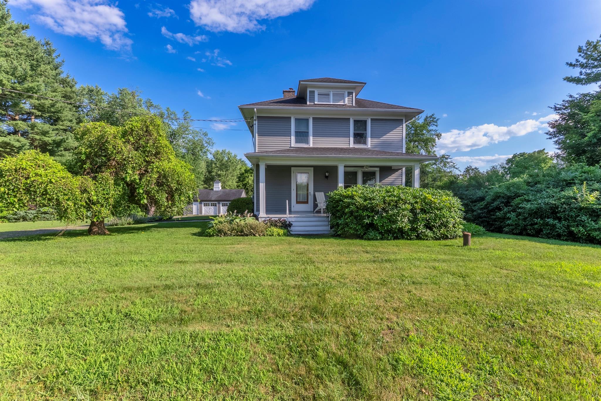 American foursquare style home with covered porch, a front lawn, and a chimney