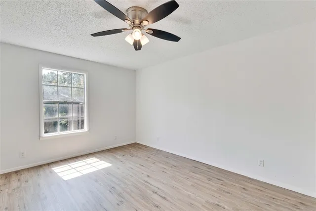 an empty room with wooden floor chandelier fan and windows