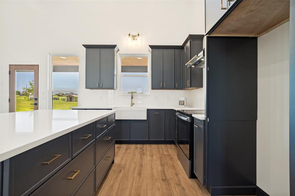 1150 Doss Road Millsap, TX 76066 - Photo 9 of 32 Modern kitchen featuring dark cabinetry, white countertops, wood-finish flooring, a farmhouse sink, and stainless steel appliances