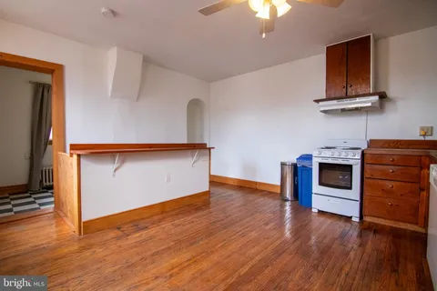 a view of an empty room with wooden floor and a kitchen