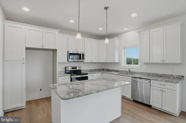 a kitchen with stainless steel appliances granite countertop a sink a stove a refrigerator and white cabinets