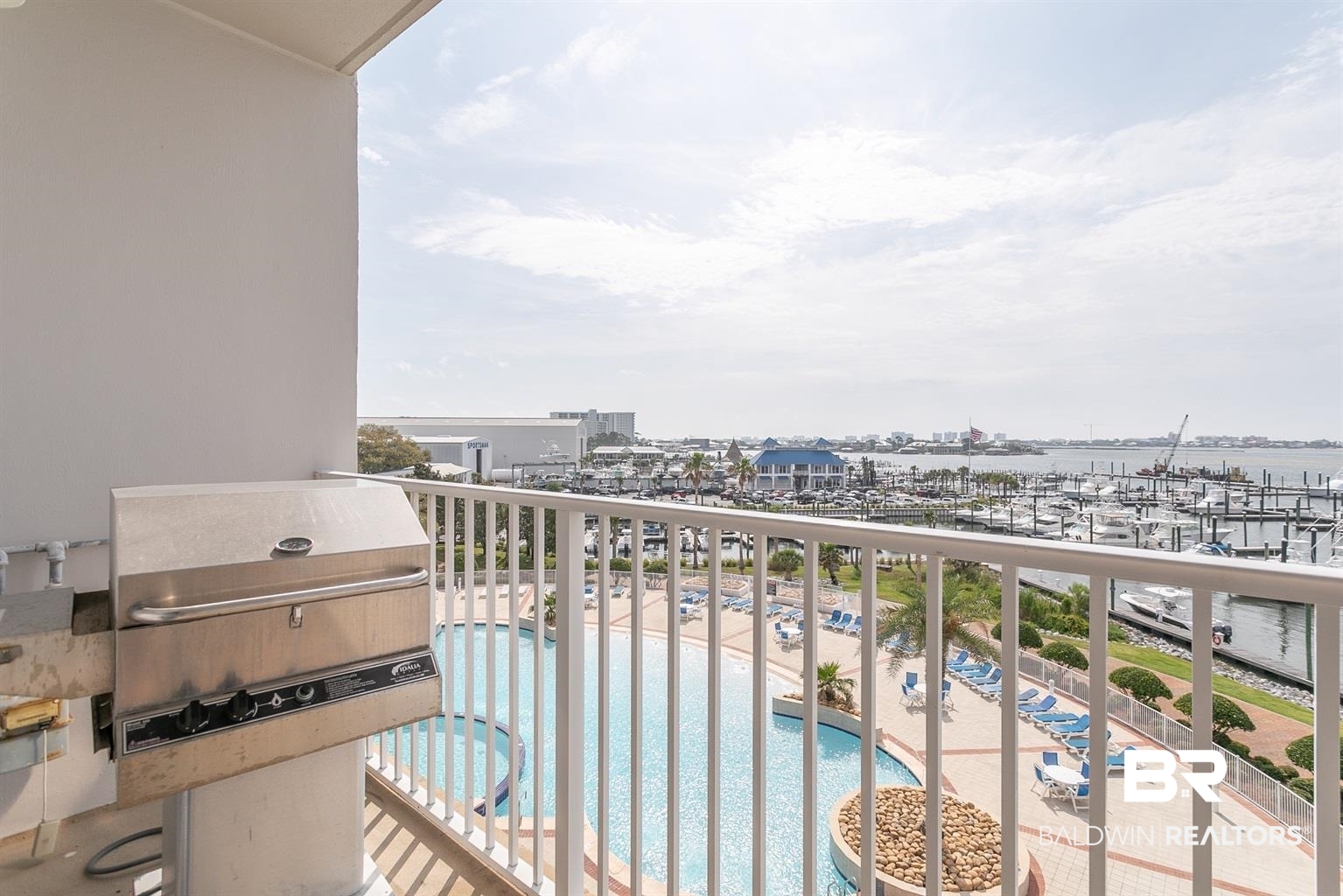27800 Canal Road, Unit 411 Orange Beach, AL 36561 - Photo 35 of 49 Balcony featuring a built-in stainless steel grill, overlooking a swimming pool with a surrounding paved deck, and a marina with numerous boats