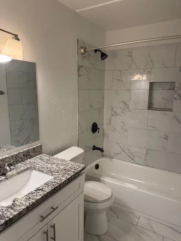 a bathroom with a granite countertop bathtub shower sink vanity and toilet