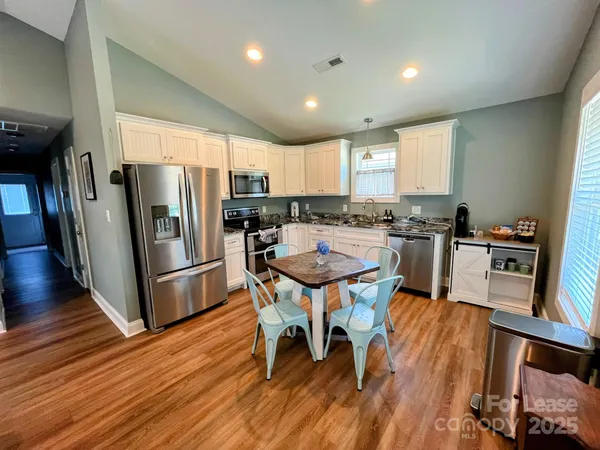 a kitchen with stainless steel appliances a dining table chairs refrigerator and sink