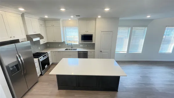 a large kitchen with stainless steel appliances a stove a refrigerator a sink a microwave and white cabinets with wooden floor