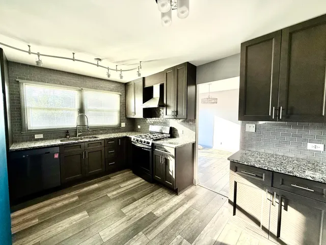 a large kitchen with granite countertop a stove top oven a sink dishwasher a dining table and chairs with wooden floor