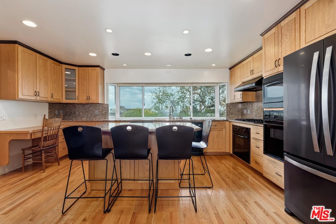 18409 Wakecrest Drive Malibu, CA 90265 - Photo 7 of 32 a kitchen with stainless steel appliances granite countertop a refrigerator a stove a sink dishwasher with a dining table and chairs with wooden floor