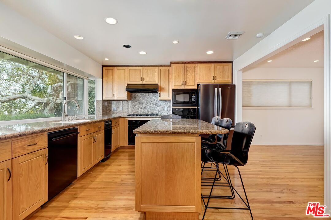 18409 Wakecrest Drive Malibu, CA 90265 - Photo 8 of 32 a kitchen with stainless steel appliances kitchen island granite countertop a table chairs in it and wooden floors