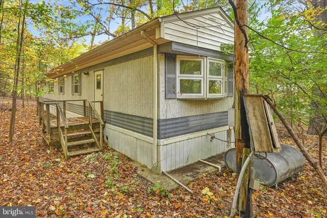 a view of a small house with wooden fence and large trees
