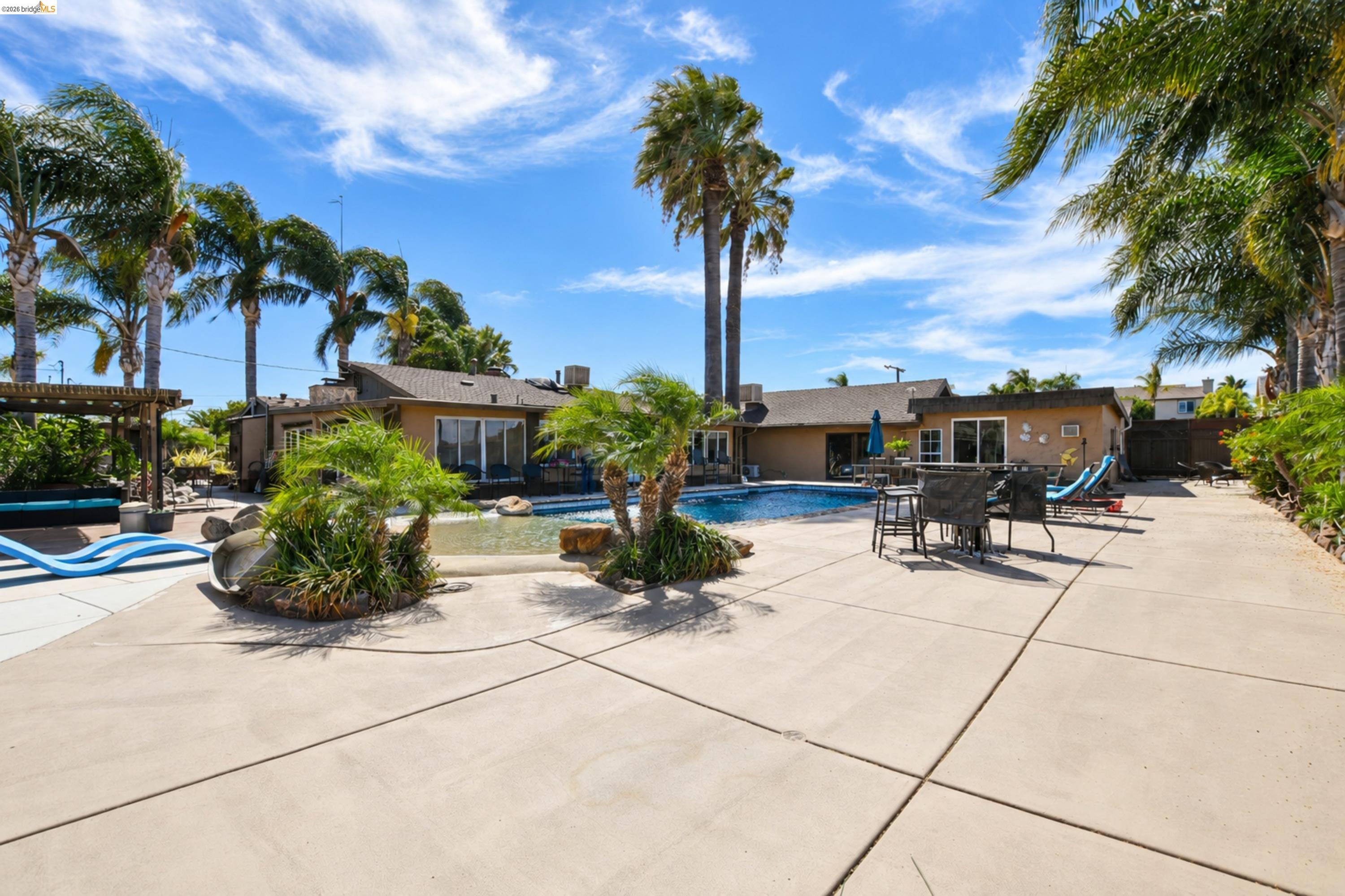 340 West Bolton Road Oakley, CA 94561 - Photo 63 of 87 Expansive concrete patio with a built-in swimming pool featuring a waterfall, surrounded by mature palm trees and lush landscaping