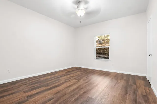 an empty room with wooden floor chandelier fan and windows