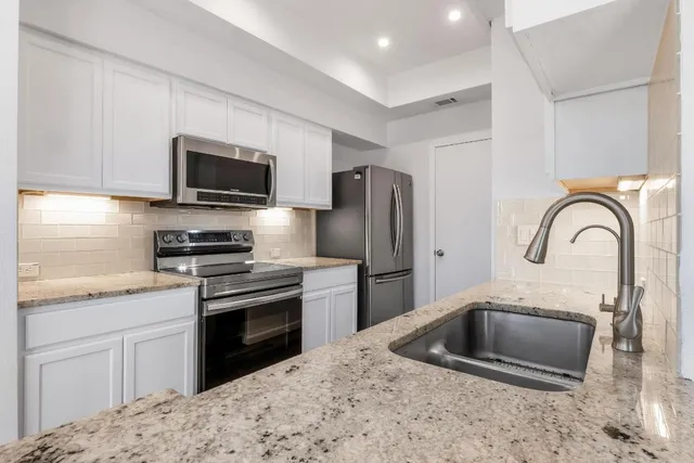 a kitchen with stainless steel appliances granite countertop a sink a stove a refrigerator cabinets and a counter top space