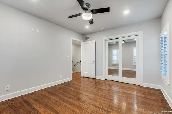 an empty room with wooden floor ceiling fan and windows
