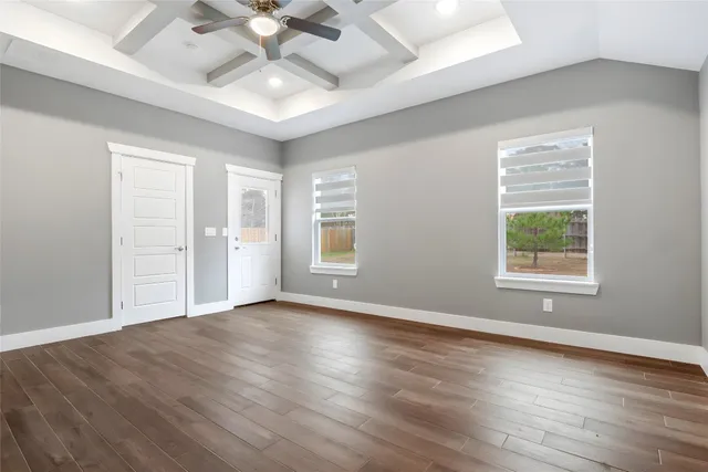 an empty room with wooden floor chandelier fan and windows