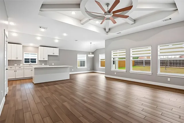 a view of an empty room with wooden floor and a kitchen