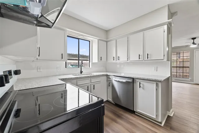 a kitchen with stainless steel appliances granite countertop a sink dishwasher a stove and white cabinets with wooden floor