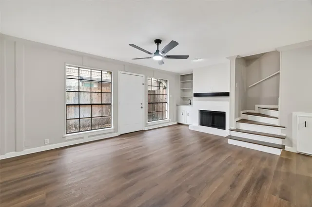 an empty room with wooden floor a ceiling fan and windows