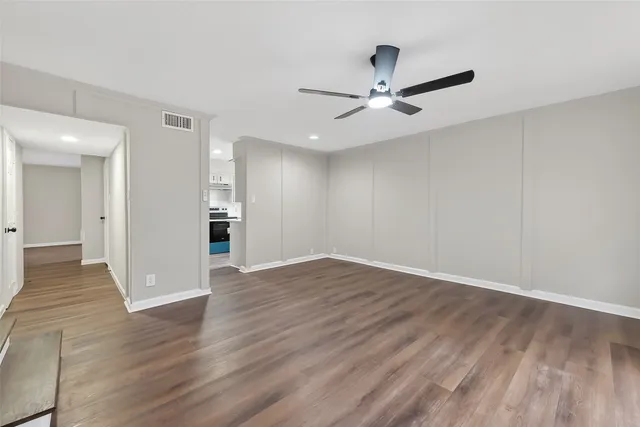 a view of an empty room with wooden floor and a ceiling fan