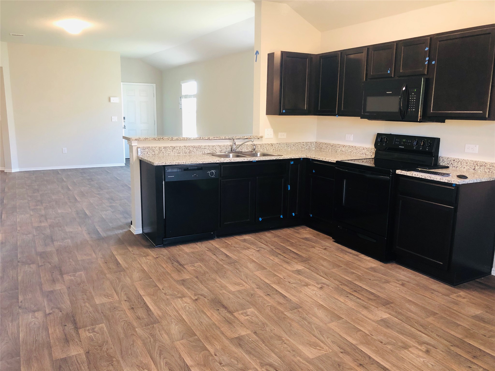 5712 Ronee Leah Drive Austin, TX 78724 - Photo 5 of 14 The kitchen features dark cabinetry, light speckled countertops, and black appliances including a dishwasher, range, and microwave