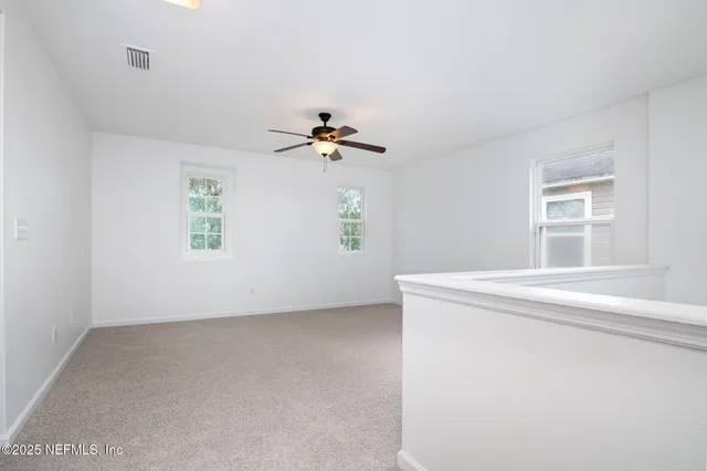 an empty room with windows and chandelier fan