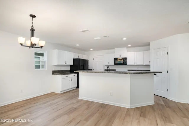 a kitchen with stainless steel appliances granite countertop a sink a stove top oven a refrigerator and white cabinets with wooden floor