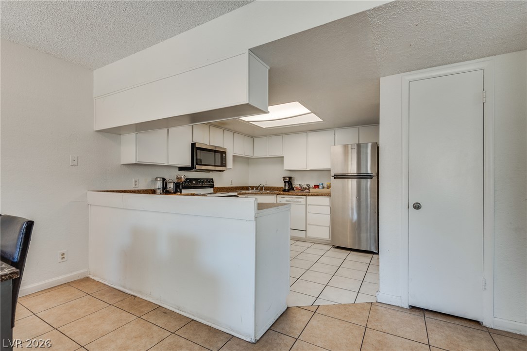 5829 Smoke Ranch Road, Unit D Las Vegas, NV 89108 - Photo 13 of 27 Tiled flooring and a raised breakfast bar define this open-plan kitchen layout.