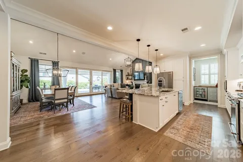 a kitchen with stainless steel appliances kitchen island granite countertop a refrigerator a stove a sink a dining table and chairs with wooden floor