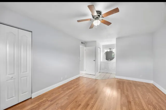 a view of an empty room with wooden floor and a ceiling fan