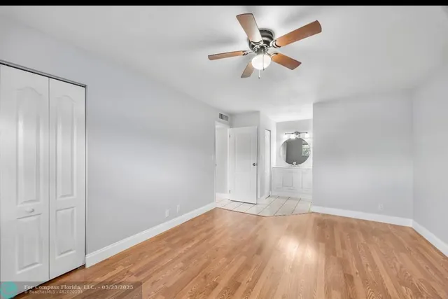 a view of an empty room with wooden floor and a ceiling fan