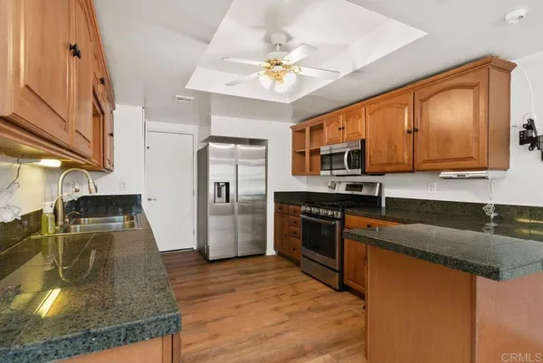 a kitchen with stainless steel appliances granite countertop a sink a stove top oven a chimney with wooden floor and cabinets