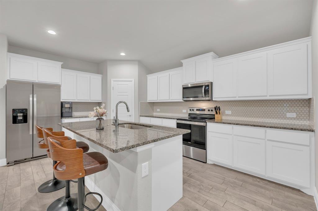 728 Golden Gate Pk Road Alvarado, TX 76009 - Photo 5 of 23 Kitchen featuring decorative backsplash, stainless steel appliances, light stone countertops, white cabinetry, and a kitchen breakfast bar