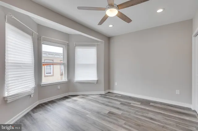 an empty room with wooden floor fan and windows