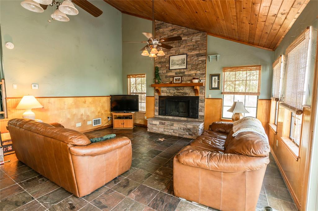 698 Storey Road Nocona, TX 76255 - Photo 33 of 34 Living room featuring a wainscoted wall, wood walls, wood ceiling, a fireplace, and stone tile flooring