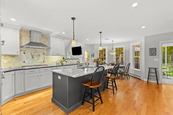 a kitchen with stainless steel appliances granite countertop a stove a sink a microwave a dining table and chairs with wooden floor